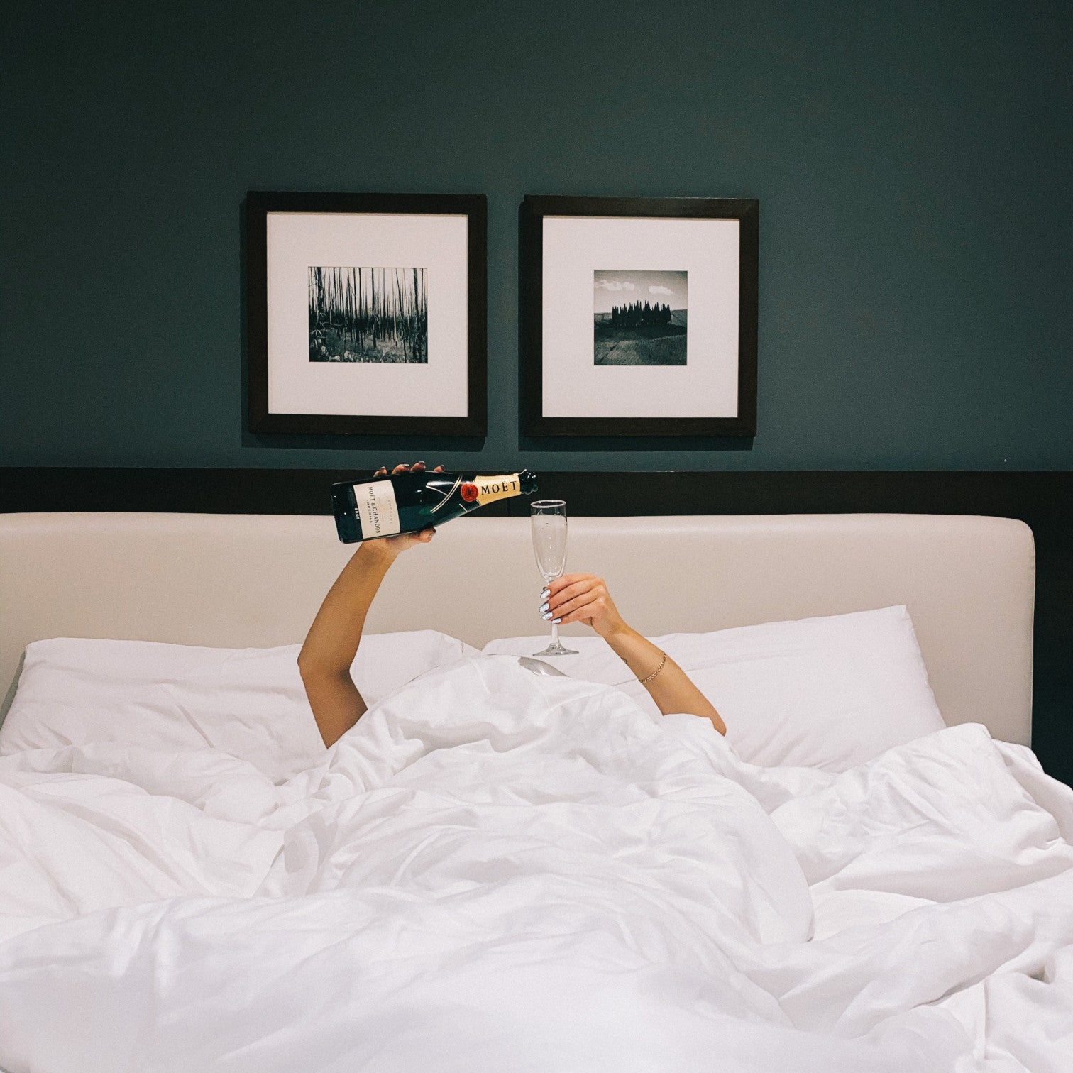 frau im bett und hät sektglas und champagner hoch